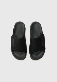Sorte slidesandaler med en myk semsket stropp som har merket "HUGO" i et subtilt, preget design. Teksturet såle i svart gummi.