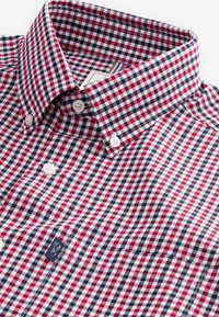 Chemise à col boutonné avec un motif à carreaux rouge, bleu marine et blanc et des boutons blancs, avec une petite étiquette bleu marine cousue en blanc.