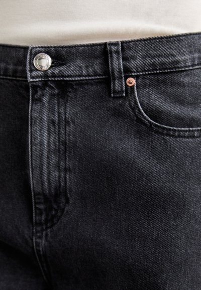 Black denim jeans with a smooth texture, featuring a silver button, copper rivet, and standard pockets, showcasing a classic design.