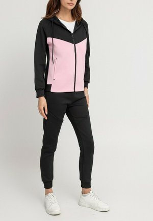 Ensemble de survêtement avec un design en blocs de couleurs noir et rose. La veste possède une fermeture éclair, une capuche et des poches avant ; le pantalon est ajusté avec des poignets côtelés.