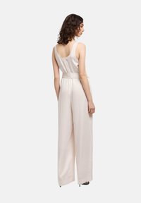 Mono de color beige claro con un top ajustado, pantalones de pierna ancha y un cinturón texturizado. Tejido suave con un diseño de espalda baja y tirantes ajustables.
