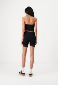 Black strapless top paired with high-waisted black shorts featuring lace trim. Model wearing black and white sneakers. Smooth texture.