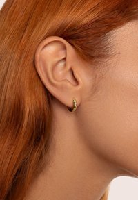 Boucle d'oreille en or avec une finition lisse et brillante, agrémentée d'un petit bijou. Portée dans une oreille percée, mettant en valeur son design élégant et arrondi.