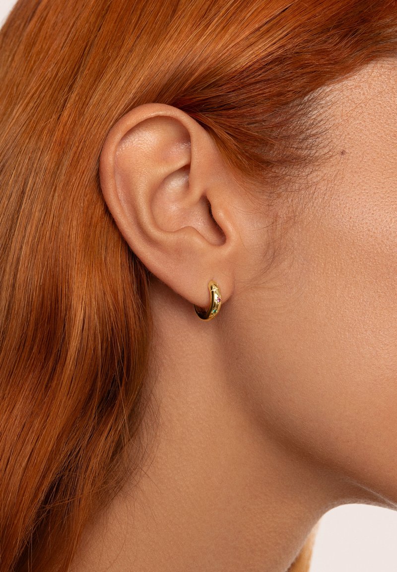 Boucle d'oreille en or avec une finition lisse et brillante, agrémentée d'un petit bijou. Portée dans une oreille percée, mettant en valeur son design élégant et arrondi.
