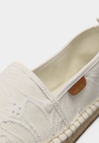 Λευκό παπούτσι εσπαντρίγια με κεντητό λουλουδένιο σχέδιο, σόλα από γιούτα και εσωτερική ταμπέλα από καφέ ύφασμα που δείχνει μερικό όνομα της μάρκας.