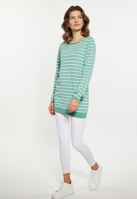 Tunika z długim rękawem z bawełny w kolorze teal z białymi poziomymi paskami, w zestawieniu z białymi spodniami slim-fit i białymi trampkami. Prosty okrągły dekolt.
