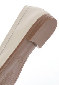Scarpa sintetica beige con tacco basso, punta arrotondata e superficie liscia. Presenta una suola in gomma marrone con logo e linee orizzontali.