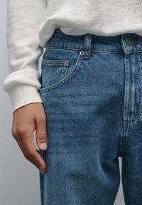 Jeans in denim blu con un classico design a cinque tasche, caratterizzati da leggeri segni di usura e dettagli di cucitura a contrasto. Il tessuto appare morbido.