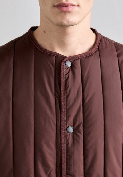 Brown quilted jacket featuring a round collar, front snap closures, and a smooth texture with vertical stitching patterns.