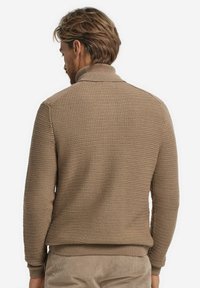 Beige stickad tröja med en texturerad yta, ribbad krage och ärmslut, samt en något avslappnad passform, med en rundad nederkant baktill.