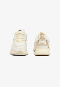 Witte en crèmekleurige sneakers hebben een glad leren bovenwerk, textuuraccenten, platte ronde veters en een gewatteerde zool met een gebogen ontwerp.