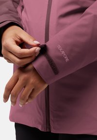 Bordeaux waterdichte jas met klittenbandverstelling bij de mouwen, voorzien van een gladde textuur en ritsluiting, gelabeld met "TEXAPORE."