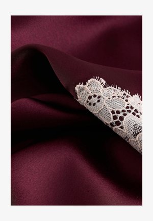 Bordová saténová látka s hladkou textúrou, zdobená jemnou bielou čipkou pozdĺž okraja, ktorá zvýrazňuje zložité vzory.