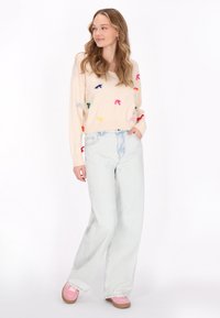 Maglione crema con fiocchi ricamati colorati, abbinato a jeans a gamba larga in denim chiaro e sneakers rosa.