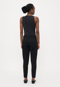 Zwarte mouwloze top gecombineerd met zwarte op maat gemaakte broek, voorzien van een riem in de taille en strakke, glanzende zwarte schoenen met een strikdetail.