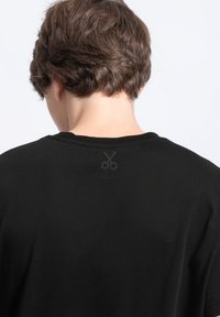 Zwarte katoenen T-shirt met een ronde hals en korte mouwen, met een subtiele schaarlogo gedrukt op de bovenrug.