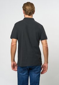 Polo gris foncé avec col, manches courtes et fentes sur les côtés, associé à un jean bleu. Tissu texturé avec des lignes épurées.