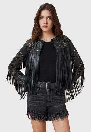 Zwarte leren jas met franjes, studded accenten, ronde halslijn, gecombineerd met een zwart topje en afgeknipte zwarte denim shorts.