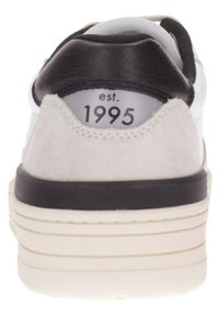 Zapatilla con talón de cuero negro, acentos de ante gris, cuerpo de cuero blanco y suela blanca elevada. Presenta "est. 1995" en la etiqueta del talón.