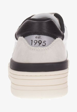 Zapatilla blanca con talón de gamuza gris y acentos de cuero negro. Presenta una suela blanca con ranuras horizontales y "est. 1995" impreso en el talón.