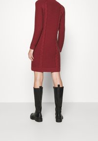 Robe tricotée bordeaux à côtes avec des détails en tricot torsadé, manches longues et col montant, associée à des bottes noires au genou.