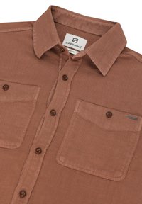 Rjava srajca na gumbe iz teksturirane tkanine. Ima ovratnik, dva žepa na prsih ter rjave gumbe z majhno oznako na desnem žepu.