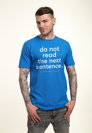 Niebieska bawełniana koszulka z wyraźnym białym napisem: "nie czytaj następnego zdania." Krótkie rękawy, okrągły dekolt, w połączeniu z przetartymi dżinsami.