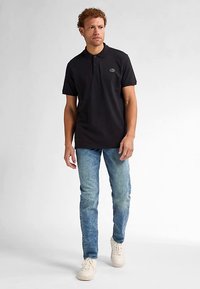 Černé polo tričko se tříknoflíkovou légou a nenápadným logem na hrudi. Kombinováno s světle modrými džínami a bílými teniskami.