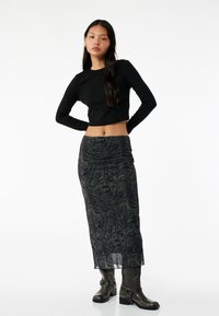 Zwarte lange mouwen crop top gecombineerd met een gestreepte groene en zwarte maxi rok, met een aansluitende taille en een zijdrape, gedragen met grijze enkelboots.