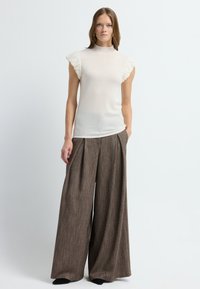 Débardeur ajusté en crème avec des accents de manches froncées, associé à un pantalon large en tissu texturé marron. Design simple sans motifs ni matériels visibles.