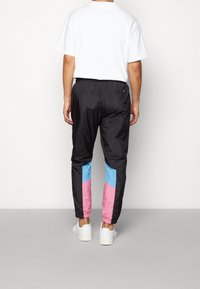 Svarta träningsbyxor för män med ljusblå och rosa paneler på sidorna, elastisk midja och en smal passform, tillverkade av ett mjukt, lätt material.