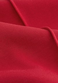 Czerwony materiał zasłonowy o gładkiej fakturze, w jednolitym kolorze z delikatnym połyskiem i gładkim, równym splocie. Brak widocznych wzorów lub akcesoriów.