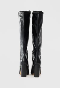 Black knee-high leather boots with block heels, back view showing vertical stitching and side zippers against a plain background.