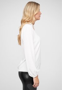 Maglietta bianca a maniche lunghe con una vestibilità comoda, caratterizzata da un collo rotondo e leggero volume alle maniche, abbinata a leggings neri.