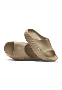 Sandalias tipo slip-on de Nike en plástico beige claro, con punta abierta, textura suave, forma curva y detalles acanalados en los laterales.