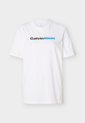 Valge lühikeste varrukatega T-särk, mille rinnale on mustade ja siniste tähtedega trükitud "Calvin Klein" logo.