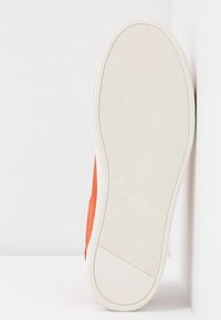 Oranžová podrážka z broušené kůže s texturovaným bílým gumovým spodkem. Obsahuje jemný detail značky a čistý, minimalistický design.