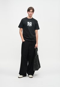 Czarny bawełniany t-shirt z białym nadrukiem, zestawiony z luźnymi czarnymi spodniami i czarną torbą na ramię. Dopełnieniem stroju są białe trampki.