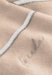 Zachte roze fleece deken met zilveren borduursels en een witte decoratieve rand langs de rand, wat contrast creëert met de stof.