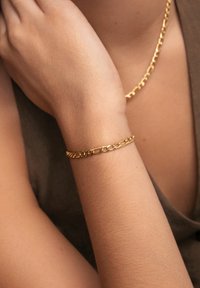 Goldene Kettenarmband mit ineinandergreifenden Gliedern, glatte Textur, am Handgelenk getragen, kombiniert mit einer passenden goldenen Halskette.