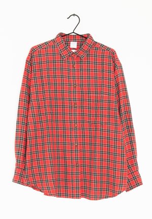 Chemise à manches longues à carreaux rouges, noirs et blancs, boutonnée, suspendue sur un cintre noir contre un fond blanc.