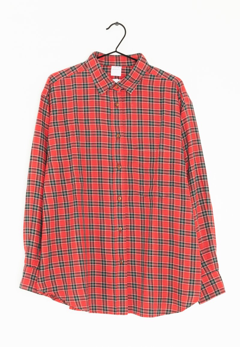 Chemise à manches longues à carreaux rouges, noirs et blancs, boutonnée, suspendue sur un cintre noir contre un fond blanc.