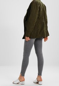 Giacca leggera verde oliva con vita rivolta, spalline e abbinate a jeans grigi aderenti e tacchi aperti argento.