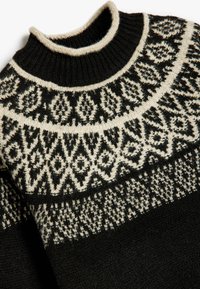 Maglione nero in lana con un motivo a crema sullo scollo. Il design include forme geometriche e dettagli lungo il colletto e il corpo.