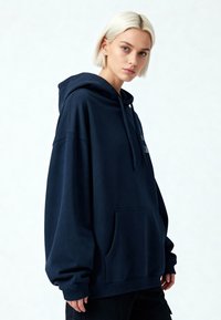 Felpa blu navy over-size realizzata in tessuto morbido, con tasca a marsupio, cappuccio con cordoncino e polsini a costine. Design semplice e informale.