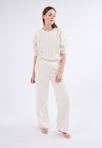 Conjunto de loungewear de color crema con un diseño de punto cableado texturizado, que incluye una sudadera de corte relajado y pantalones de pierna ancha. Tela suave y esponjosa.
