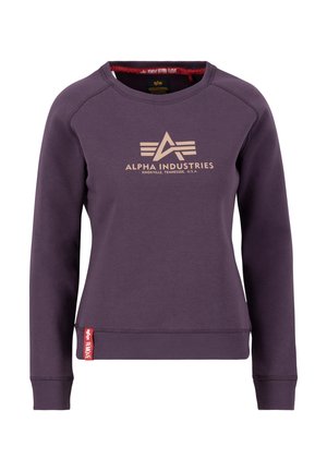Lila crewneck pulóver puha anyagból, arany színű elülső logóval és piros címkével a bal alsó szegélyen. Közepes méretű, bordázott mandzsettákkal.