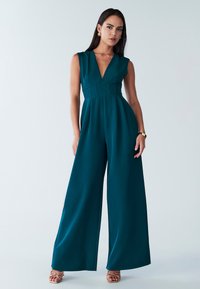 Türkisfarbener Overall mit tiefem V-Ausschnitt, ärmellosem Design und weitem Bein. Glatte Textur mit taillierter Passform und geschichtetem Detail.