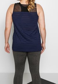 Marineblaues Tanktop mit horizontalen Streifen und transparentem schwarzem Mesh-Einsatz am Ausschnitt. Graue Leggings mit strukturierter Oberfläche vervollständigen das Outfit.