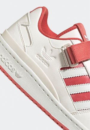 Witte en rode Adidas sneaker met drie witte strepen, klittenbandsluiting en geperst Adidas-logo op de zijkant en zool.